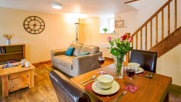 A cozy living room with a sofa, a dining table set for two, and a staircase. - 1 Bed in Bala (oc-89368) (Llandderfel)