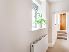 A hallway with a radiator, a potted plant on a window sill, and a wooden door at the end.