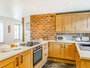 A modern kitchen with wooden cabinets, a brick accent wall, a microwave, a toaster, and a kettle.