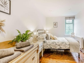 A bedroom with a bed, bedside table, lamp, and a window with a view.