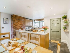 A kitchen with a brick wall, wooden cabinets, a central island, and a dining area with a table set for four.