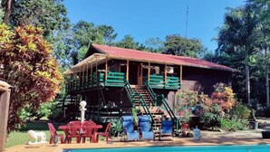 Una casa de madera con techo rojo, piscina y una escalera que lleva a un balcón.