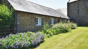 Ein Gebäude aus Stein mit einem geneigten Dach, einem Holzzaun und einem Garten mit violetten Blumen.