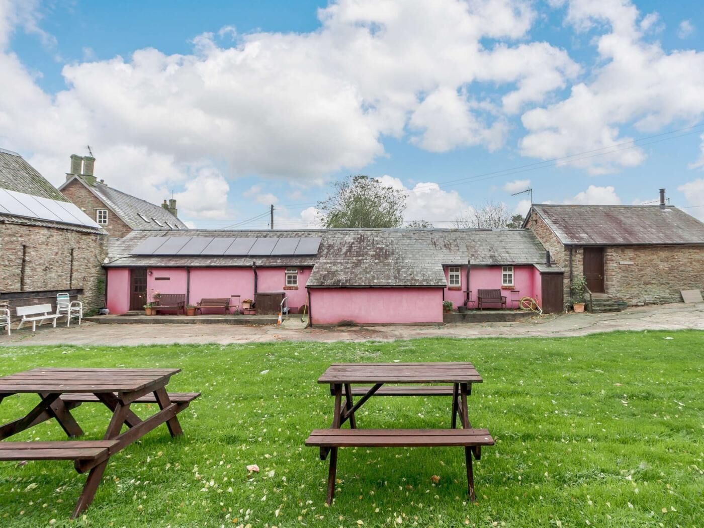 Ein rustikales Gebäude mit rosa Fassade, eine Rasenfläche mit Picknicktischen und ein klarer Himmel.