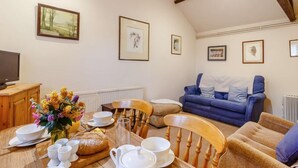 Ein gemütliches Wohnzimmer mit Esstisch, gedeckten Tellern für das Frühstück, einem blauen Sofa und gerahmten Bildern an den Wänden.