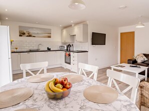 Une cuisine moderne avec des meubles blancs, un four à micro-ondes et un coin repas comprenant une table en marbre et des chaises blanches.