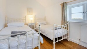 A bedroom with two beds, a nightstand with a lamp, a window with curtains, and a radiator. - 3 Bed in Newport (oc-90245) (Newport)