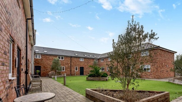 A courtyard with a brick building, a round table with chairs, and a small tree. - 3 Bed in Newport (oc-90245) (Newport)