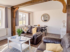 A living room with a brown leather sofa, a white coffee table, a dining table with chairs, a round mirror on the wall, and a window with curtains. - 2 Bed in Newport (oc-90244) (Newport)
