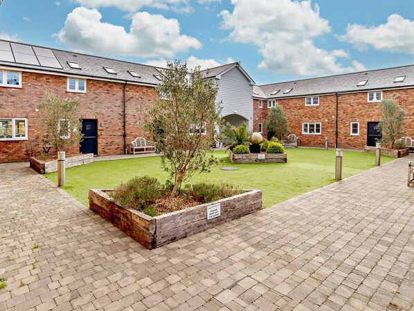 A courtyard with brick buildings, a grassy area, and wooden planters.
