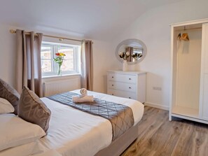 A neatly made bed with a rolled towel, a dresser with drawers, a mirror, and a window with curtains.