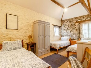 Un dormitorio con dos camas, un armario, un escritorio y una pared de piedra.