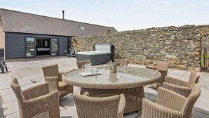 Eine Terrasse mit Korbmöbeln, einem Whirlpool und einer Steinwand.
