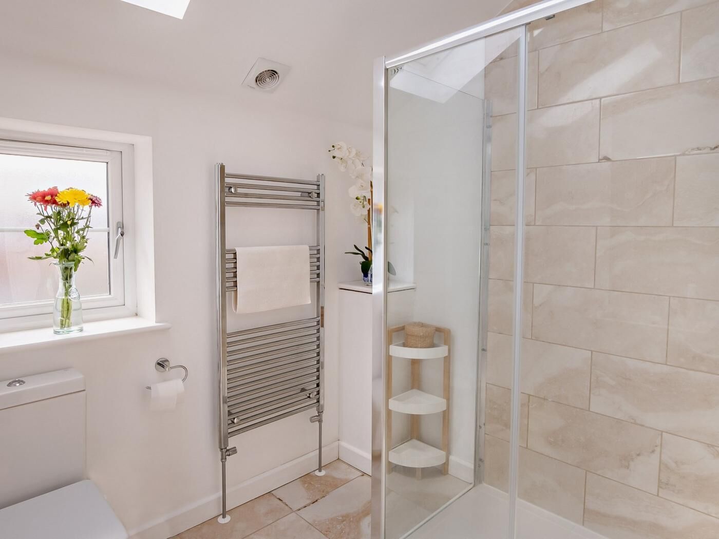Une salle de bain moderne avec une douche à parois de verre, un porte-serviettes, des toilettes et une fenêtre ornée de fleurs.