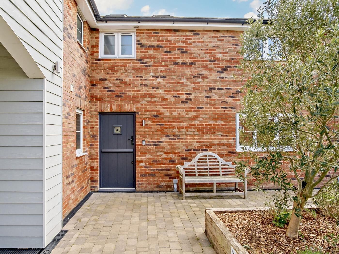 A brick house with a dark front door, a small window, and a bench.