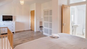 Una camera da letto con un letto, una TV sopra un comò, una culla in legno, una porta che dà su un bagno e un lampadario.