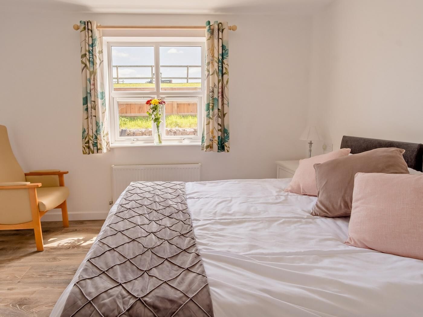 A bedroom with a bed, a chair, a window with curtains, and a radiator.