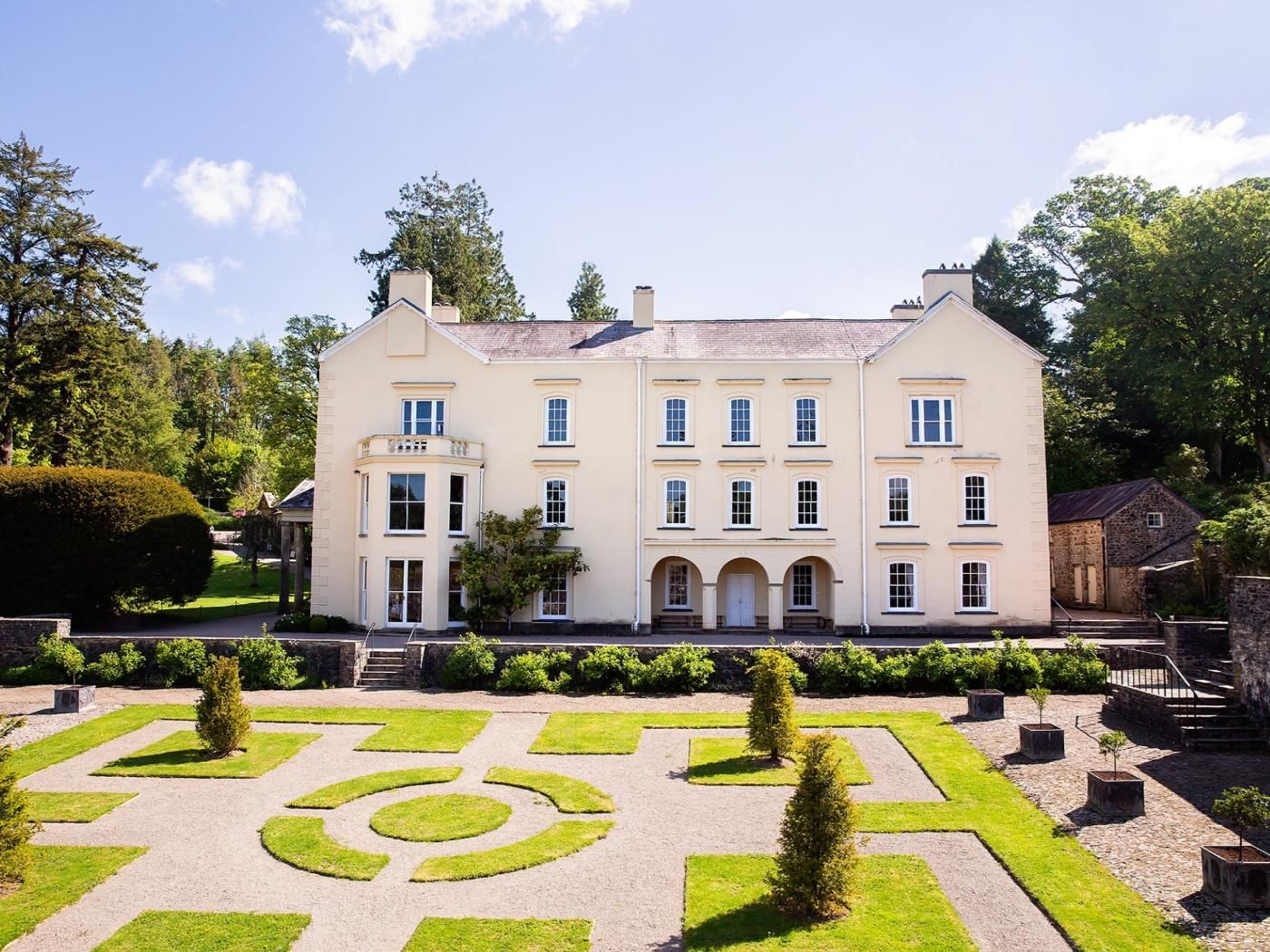 A large, multi-story building with a symmetrical facade, a central entrance with arches, and a formal garden with geometric patterns.