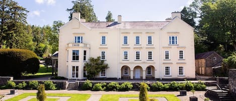 A large, multi-story building with a symmetrical facade, a central entrance with arches, and a formal garden with geometric patterns.