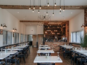 Un restaurant doté de nombreuses tables et chaises, d’un mur en briques et de luminaires suspendus.