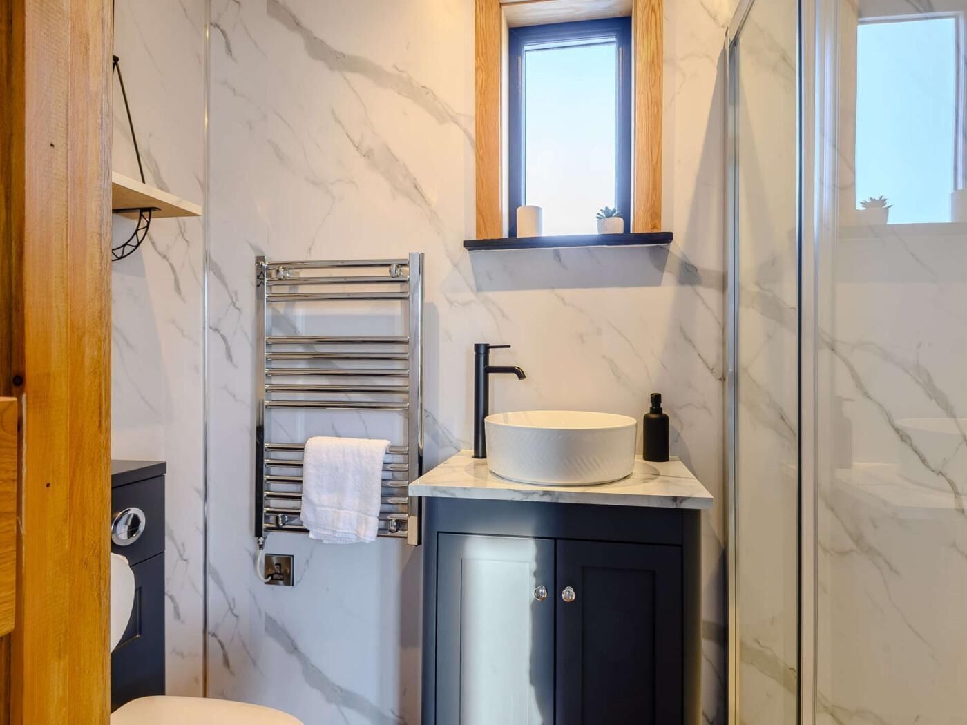 Une salle de bain avec un mur en marbre, un porte-serviettes, un lavabo avec un robinet noir et un miroir au-dessus du lavabo.