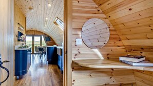 Interior em madeira com teto curvo, área de cozinha e um detalhe circular na parede.