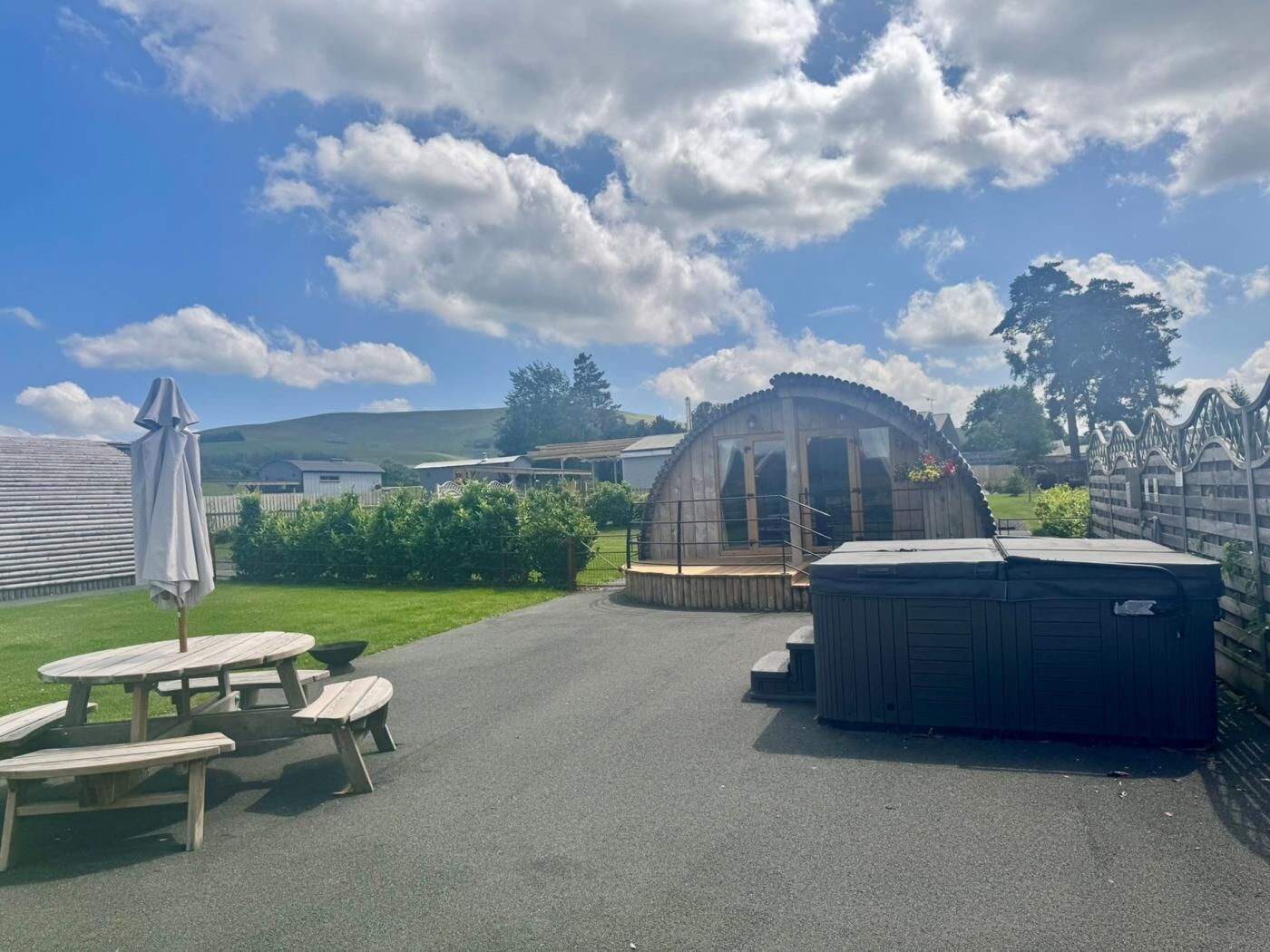 A covered outdoor area with picnic tables, a hot tub, and a greenhouse structure.
