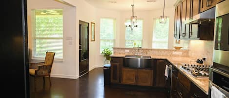 A kitchen with dark wooden cabinets, a stainless steel sink, a gas stove, and a chandelier.