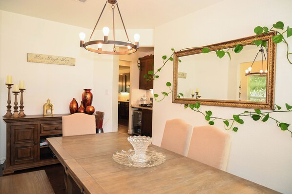 A dining area with a wooden table, chairs, a chandelier, a mirror, and decorative items.