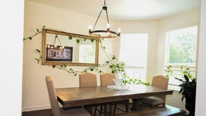 A dining area with a wooden table, four chairs, a bench, a chandelier, a mirror, and a potted plant.