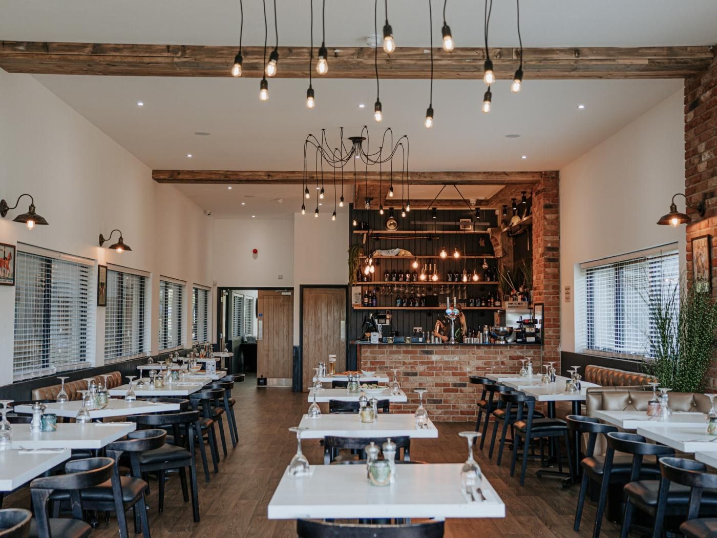 A restaurant with multiple tables and chairs, a bar area, and a brick wall.