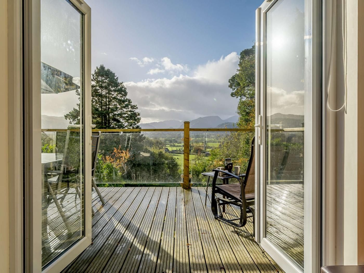En træterrasse med gelænder af glas med udsigt over et landskab med træer og bjerge.