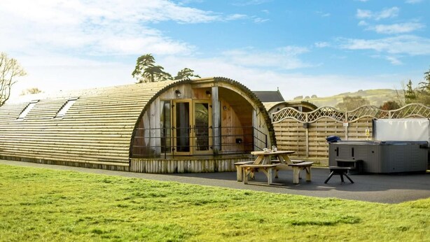 Een houten hut met een gebogen dak, een terras met tafels en stoelen, en een hottub.
