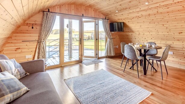 Ein gemütlicher Holzraum mit einer Couch, Esstisch, Stühlen und einem Fernseher.