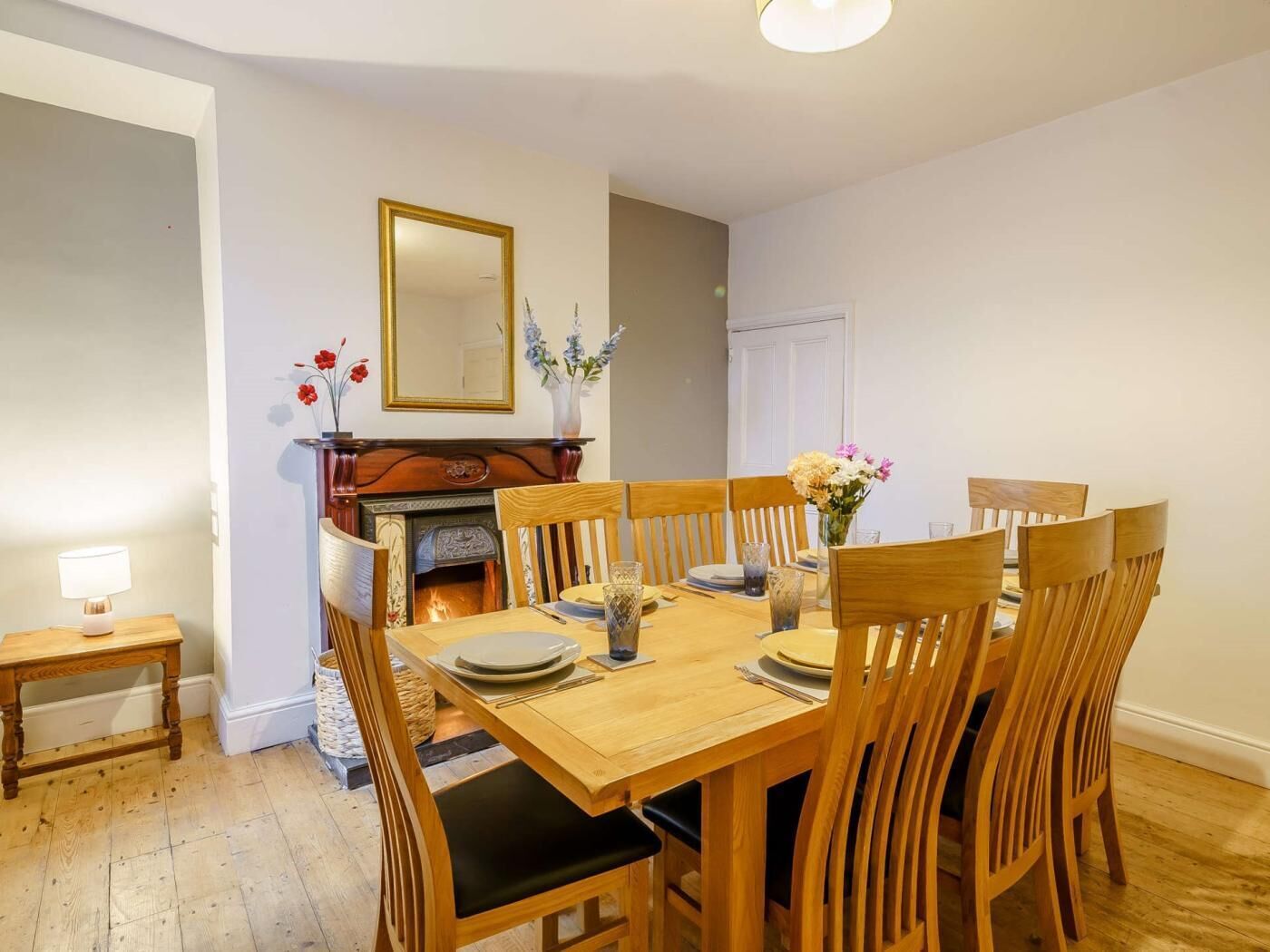 Een eetkamer met een houten tafel gedekt voor vier personen, een open haard en een spiegel aan de muur.