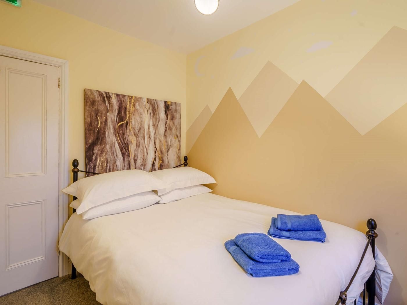A hotel room with a bed, white linens, a headboard with a marble-like design, and a wall with a geometric pattern.