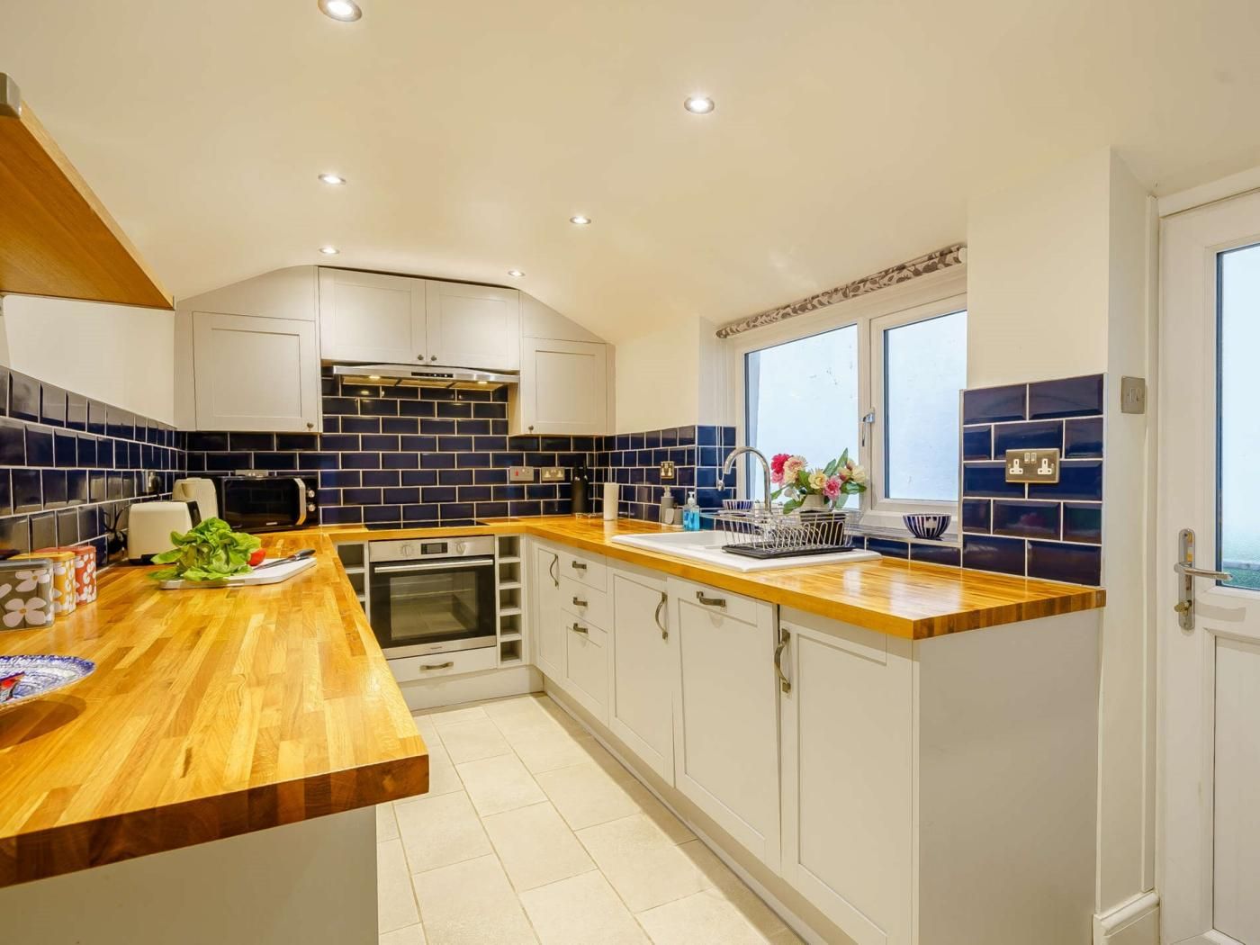 A modern kitchen with white cabinets, a wooden countertop, and a blue-tiled backsplash.