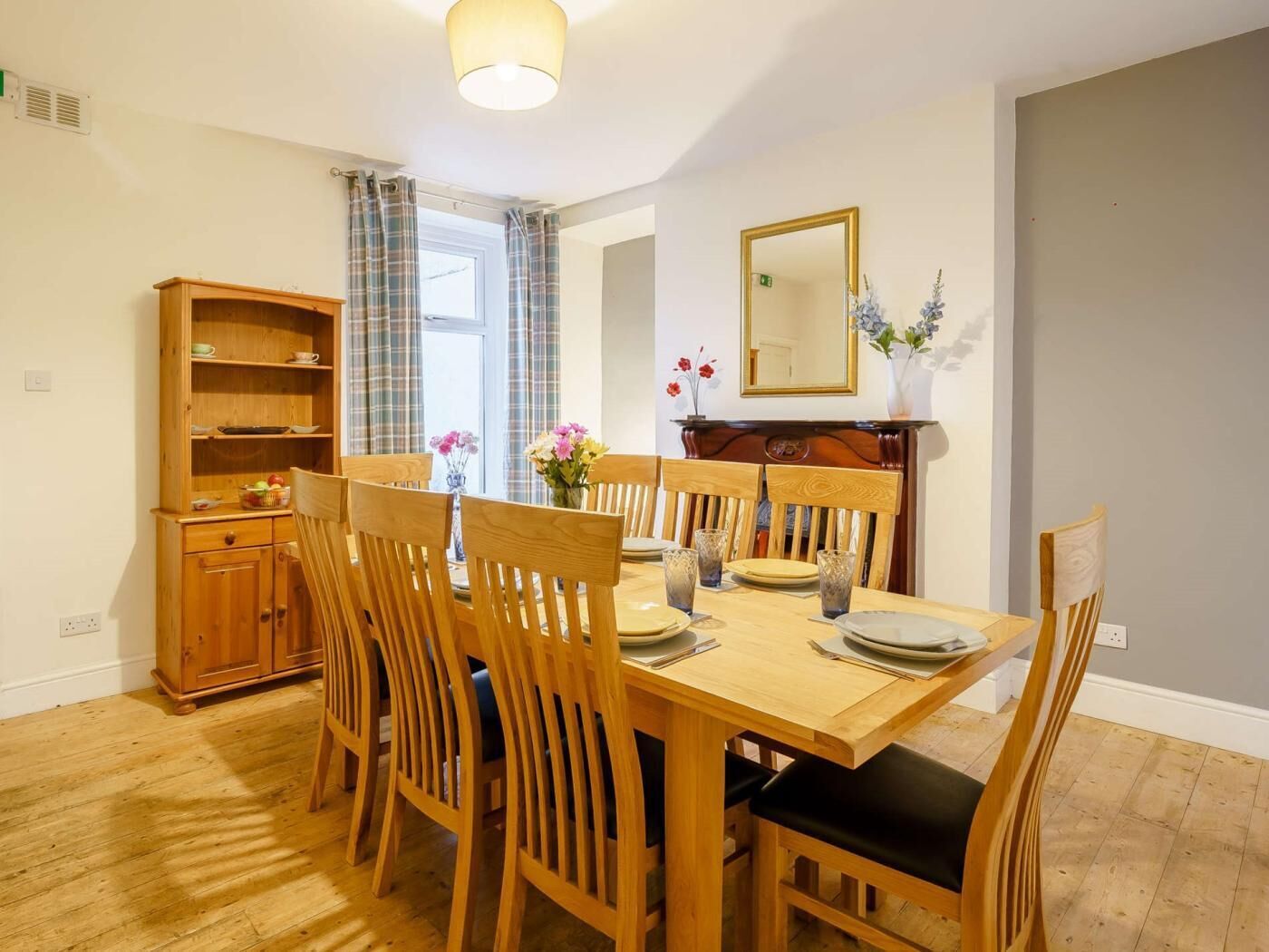 A dining area with a wooden table and chairs, a wooden cabinet, and a mirror on the wall.