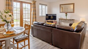 Un salon comprenant un canapé, un téléviseur, une table à manger avec des chaises et une fenêtre avec des rideaux.