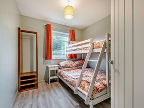 A bunk bed room with a wooden ladder, a small bedside table, and a window with curtains.