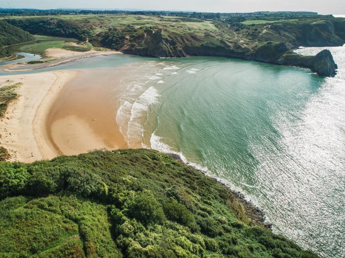 A coastal landscape with a sandy beach, a river, and green hills.