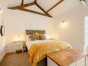 Ein Schlafzimmer mit einem Bett, Nachttischen, einer Holzbänkl und einer geneigten Decke mit freiliegenden Balken.