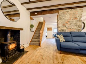 Uma sala de estar acolhedora com parede de pedra, lareira, sofá azul e escada de madeira.