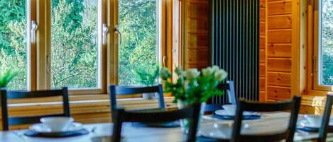 Comedor con paredes de madera, ventanas amplias y una mesa dispuesta para cuatro.