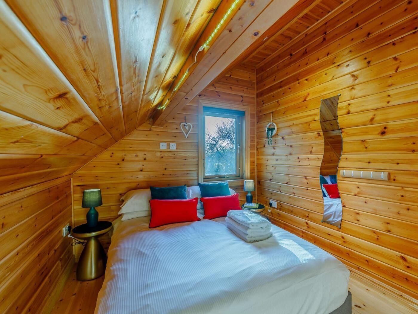 Quarto de cabana de madeira com uma cama, luminárias de cabeceira, uma janela e uma decoração em formato de coração na parede.