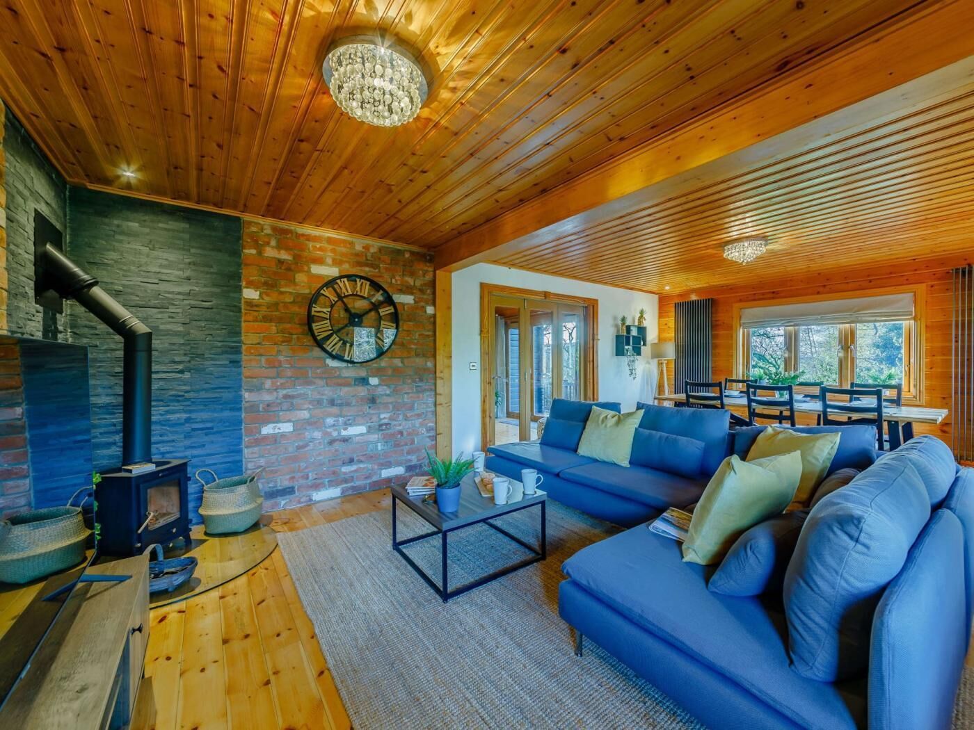 A cozy living room with a stone fireplace, a blue sofa, and a wooden ceiling.