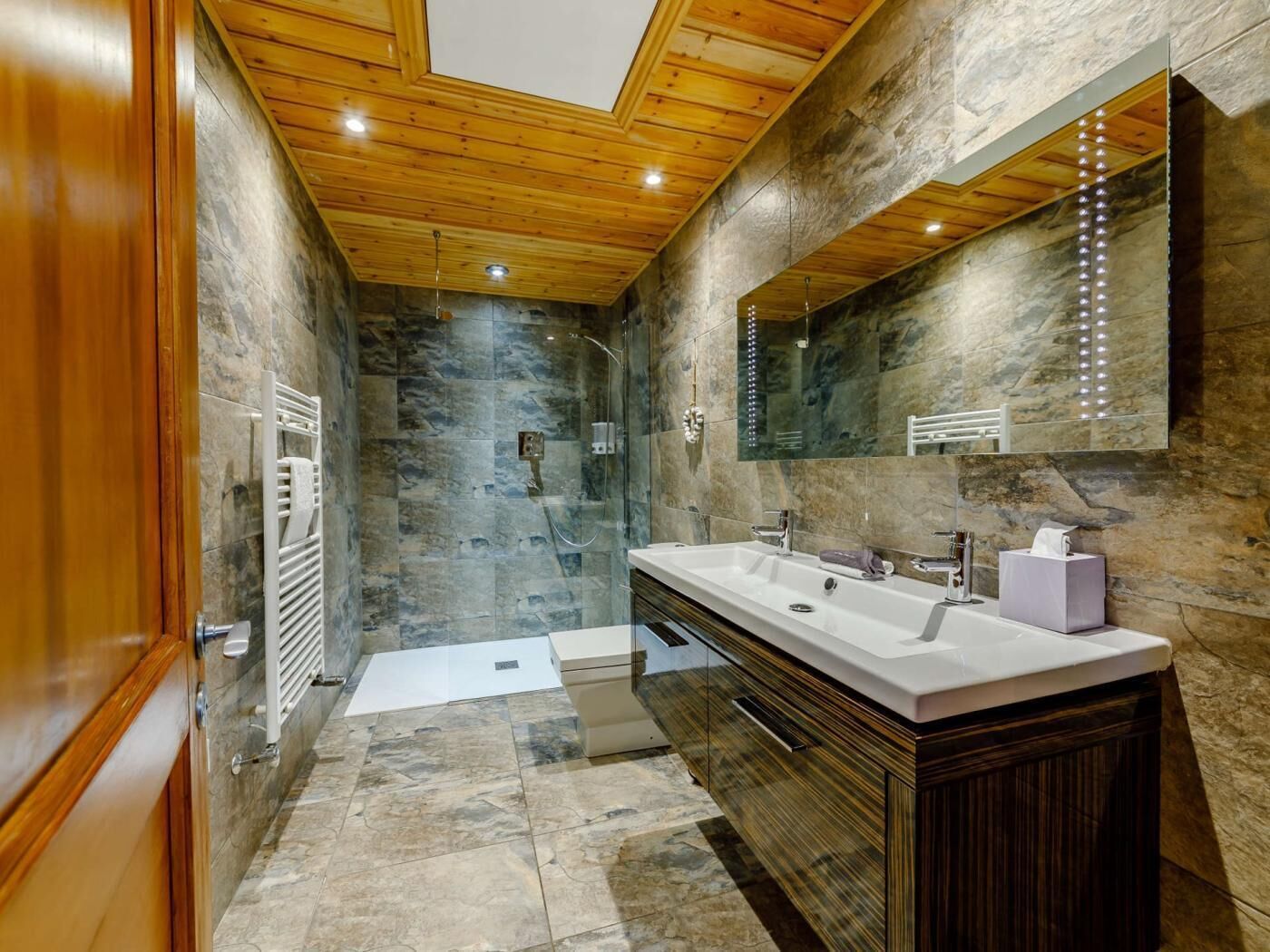 Un bagno moderno con parete in pietra, soffitto in legno e un ampio specchio.