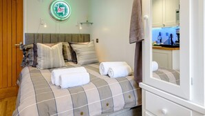 Ein Schlafzimmer mit einem Bett, Kissen, einer Uhr, einem Handtuch, einem Spiegel und Blick zur Küche.
