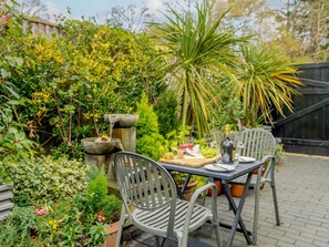 An outdoor dining area with a table set for two, surrounded by lush greenery and a small water feature. - 1 Bed in Christchurch (oc-90444) (Highcliffe)