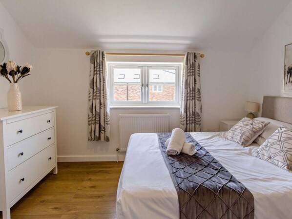 Ein Schlafzimmer mit einem Bett, einem Schminktisch, einem Fenster mit Vorhängen und einer Heizung.